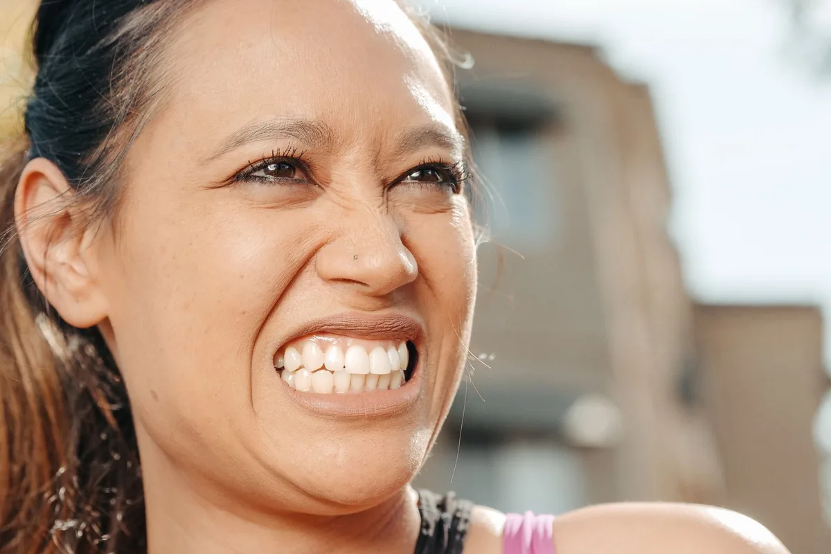 A woman laughing outdoors, head tilted back, with an open and unselfconscious smile
