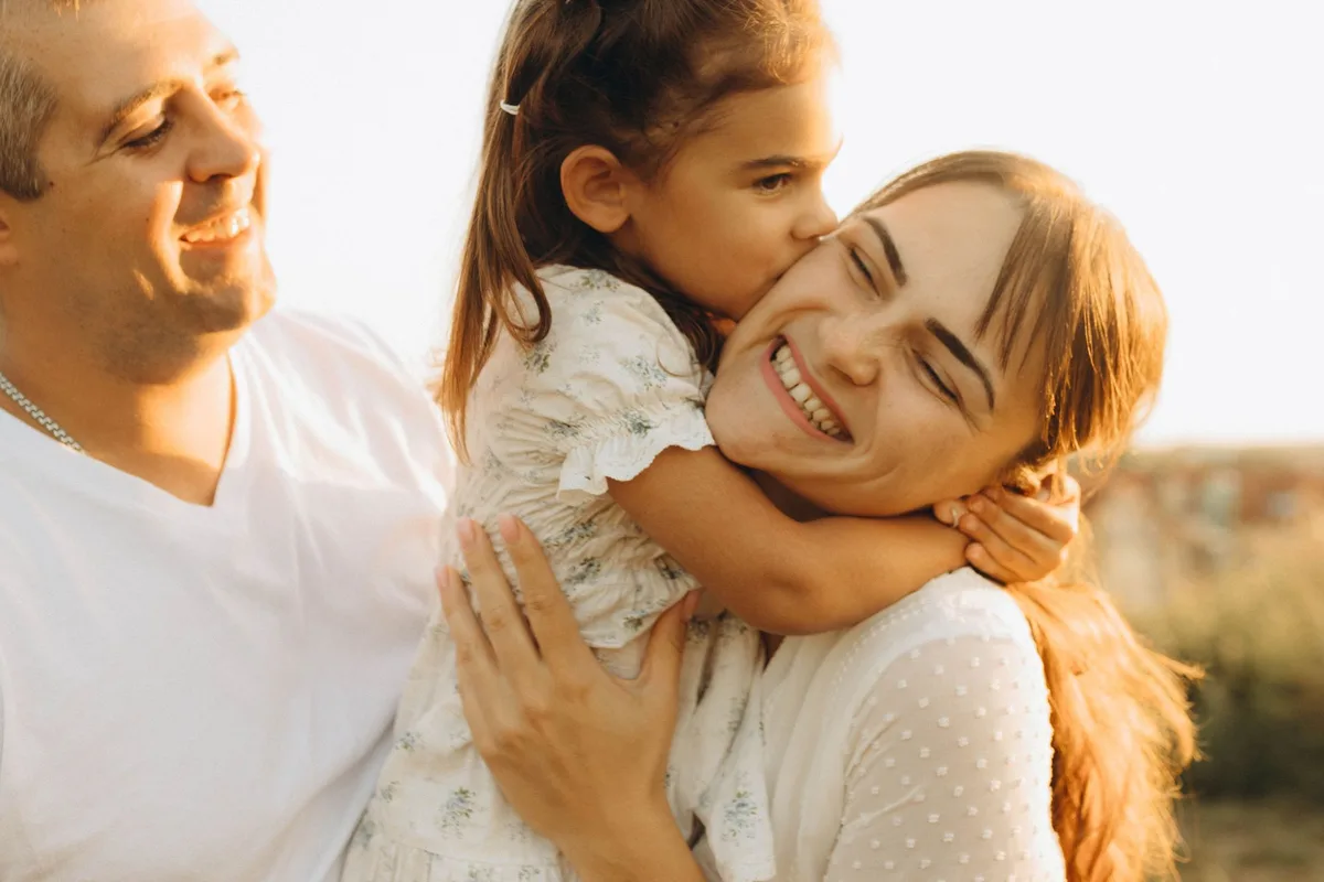 A mother, father and young daughter laughing together outdoors in the late afternoon sun