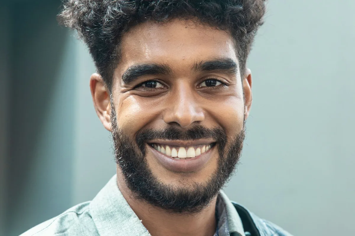 A young man with a beard grinning, lit by warm afternoon light