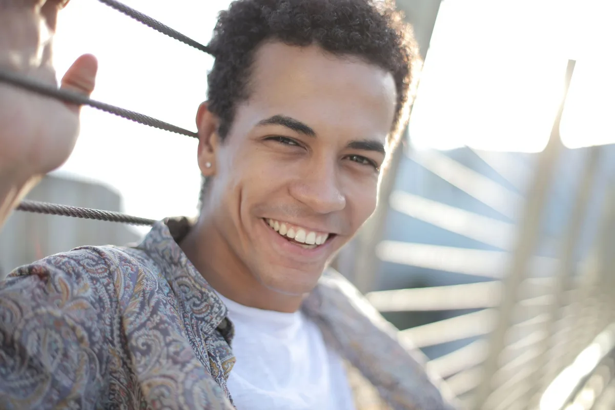 A man leaning against a railing outdoors, smiling broadly