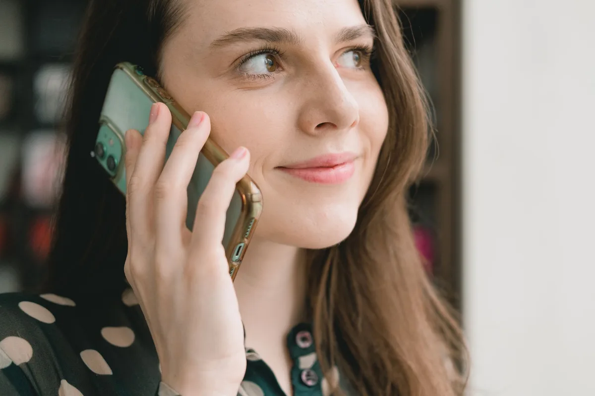 A woman holding a phone to her ear, listening calmly, in soft daylight