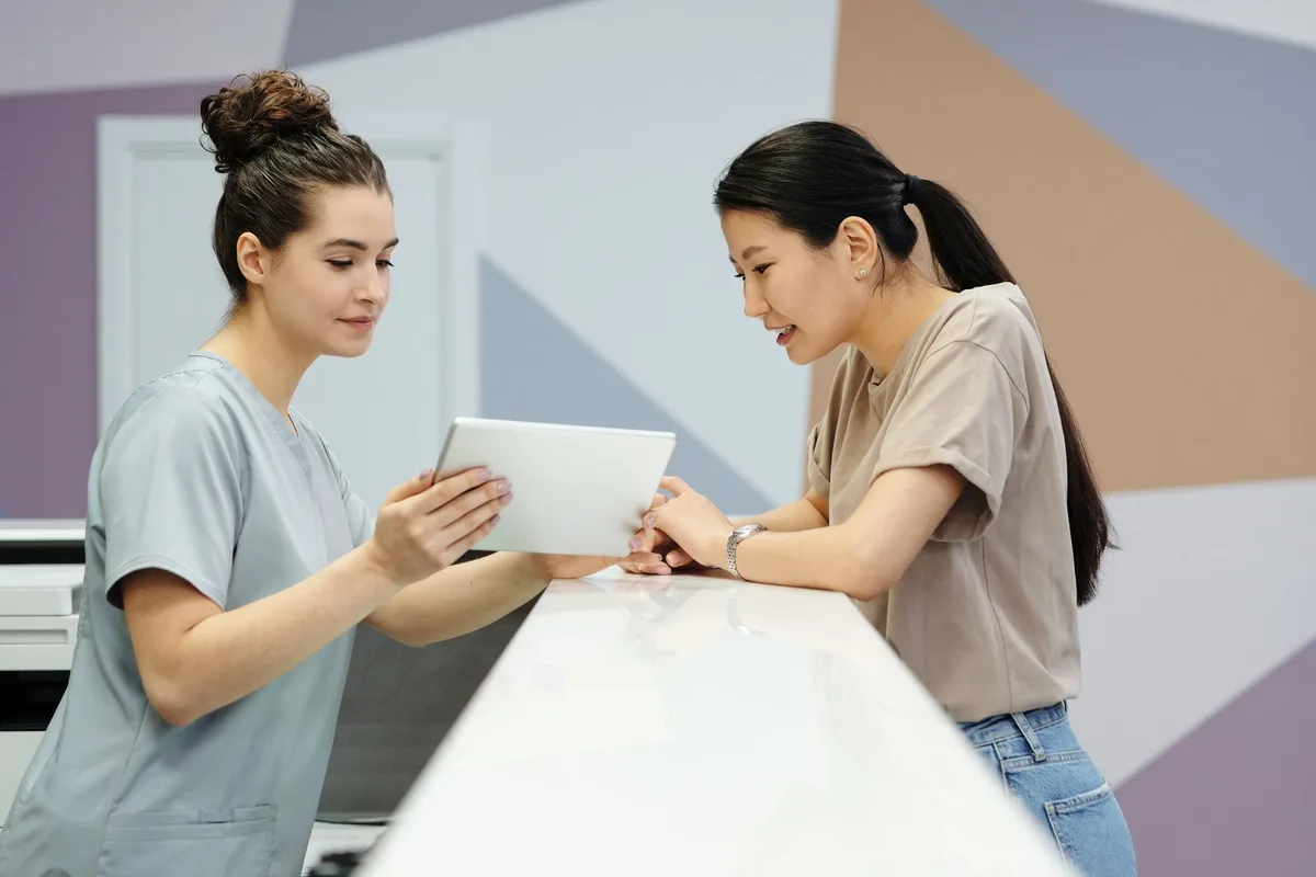 Two people talking over a tablet at a bright front desk, working something out together